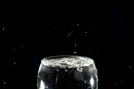 Splashing water drops in a full glass goblet. Splash Effect. Isolated on dark background.の写真素材