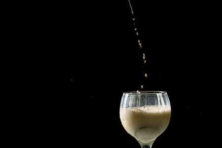 Drops of milk falling into a wine glass. Isolated on black background.の写真素材