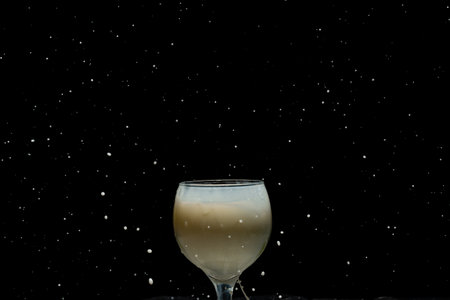 Glass wine glass with milk inside. Drops in the air against black studio background.の写真素材