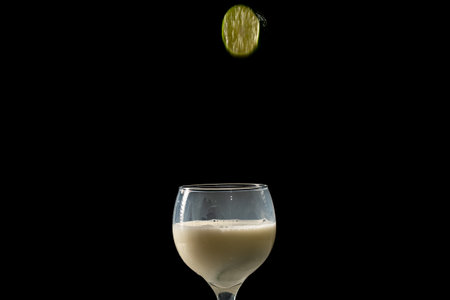 A slice of lemon falling into a glass cup with milk inside. Isolated on black background.の写真素材