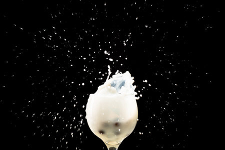 Splash in a glass bowl with milk inside. Drops in the air. Isolated on black background.の写真素材