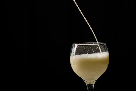 Milk falling into a glass cup. Isolated on black background.の写真素材