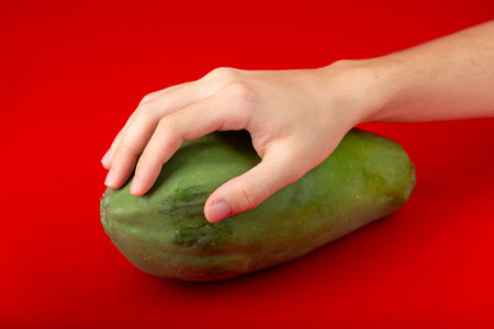 Male hand on top of a green papaya. Isolated on red background.の写真素材