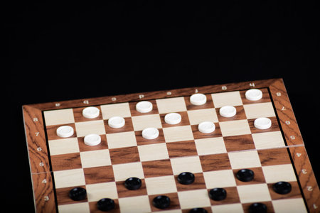 Checkerboard with light and dark pieces. Game concepts. Board game. Hobby. Checkers on the playing field for a game on a black background.の写真素材