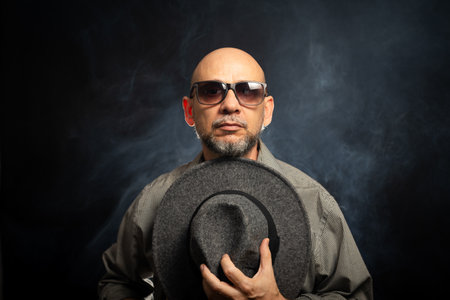 Man with a beard and sunglasses holding a gray hat. Against smoky background.の写真素材
