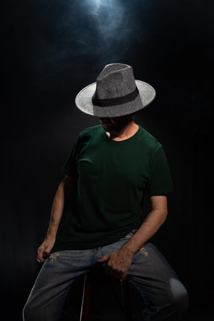 Mysterious, bearded man wearing a hat covering his face. Studio portrait. Dark background with artificial smoke.の写真素材