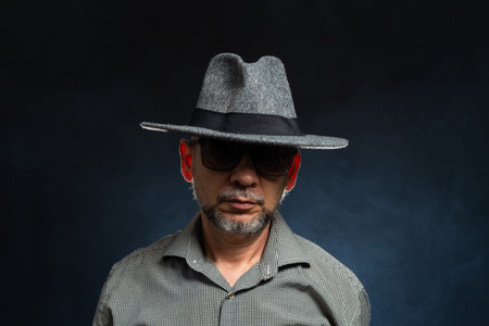 Bearded man in glasses wearing gray hat against dark background. Photo in studio.