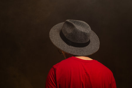 Middle-aged bearded man with his back to the camera wearing a hat and posing for the photo. Colorful studio background with artificial smoke.の写真素材