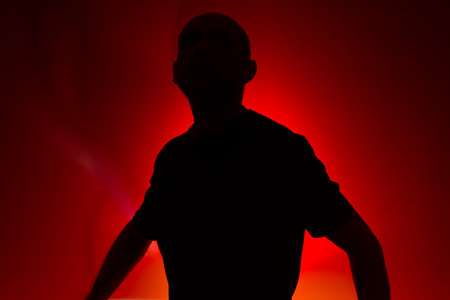 Studio portrait of a man in silhouette, standing still and posing. Isolated on red background.の写真素材