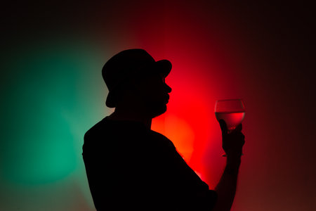 Portrait of an unidentified man in silhouette holding a glass with liquid inside. Isolated colored...