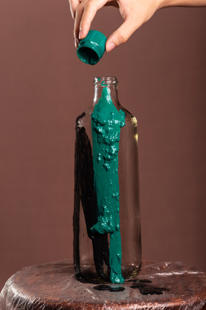 Close-up portrait of a glass bottle being painted with green paint. Abstract. Isolated on brown background.の写真素材