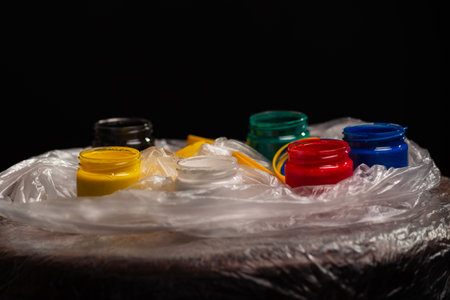 Pots of black, yellow, green, red and blue paints on top of plastic. Isolated on black background.の写真素材