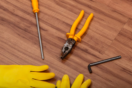 Pair of cleaning gloves, pliers, screwdriver, wrench and other tools isolated on wooden background.の写真素材