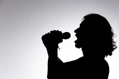 Silhouette of young man holding wireless microphone singing music with emotion. Isolated on white background.の写真素材