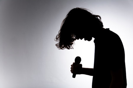 Silhouette of young man holding wireless microphone singing music with emotion. Isolated on white background.の写真素材