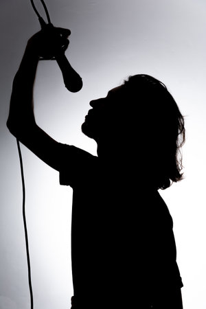 Silhouette of young singer holding wired microphone and singing with emotion. Isolated on white background.の写真素材