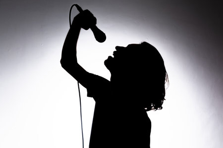 Silhouette of young singer holding wired microphone and singing with emotion. Isolated on white background.の写真素材