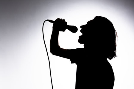 Silhouette of young singer holding wired microphone and singing with emotion. Isolated on white background.の写真素材