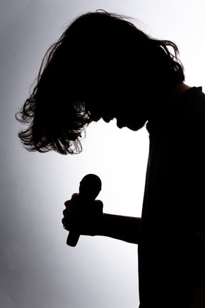 Silhouette of young man holding wireless microphone singing music with emotion. Isolated on white background.の写真素材