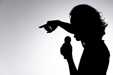 Silhouette of young man holding wireless microphone singing music with emotion. Isolated on white background.の写真素材