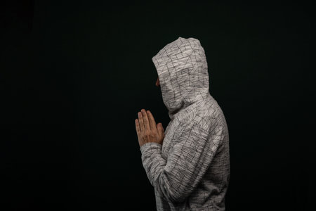 Mysterious man wearing hooded sweatshirt making hand gestures. Isolated on darkened background.の写真素材