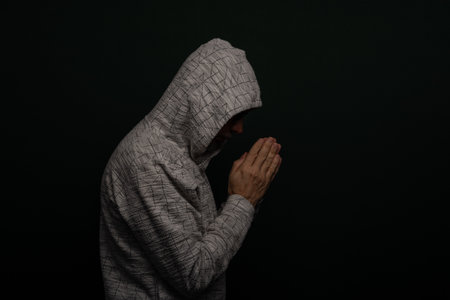 Mysterious man wearing hooded sweatshirt making hand gestures. Isolated on darkened background.の写真素材