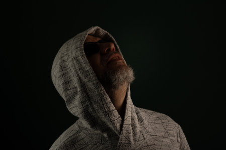 Portrait of man wearing sunglasses and hooded sweatshirt looking up. Isolated on dark background.の写真素材