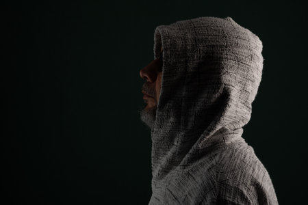 Mysterious man wearing sunglasses and hooded sweatshirt covering his head. Isolated on darkened background.の写真素材