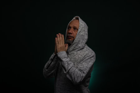 Mysterious man wearing hooded sweatshirt making hand gestures. Isolated on darkened background.の写真素材