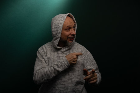 Mysterious man wearing hooded sweatshirt making hand gestures. Isolated on darkened background.の写真素材