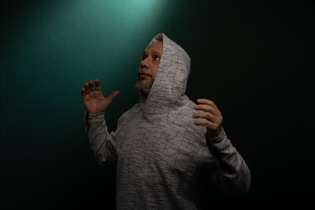 Mysterious man wearing hooded sweatshirt making hand gestures. Isolated on darkened background.の写真素材
