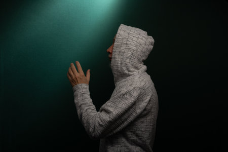 Mysterious man wearing hooded sweatshirt making hand gestures. Isolated on darkened background.の写真素材