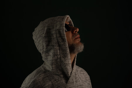 Portrait of man wearing sunglasses and hooded sweatshirt looking up. Isolated on dark background.の写真素材
