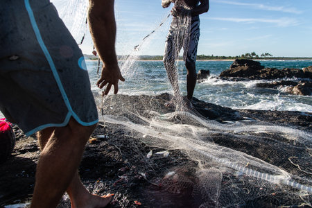 Salvador, Bahia, Brazil - December 29, 2019: Fishermen are seen on the rocks on the beach taking care of their fishing nets and fish in the city of Itacare, Bahia.のeditorial素材