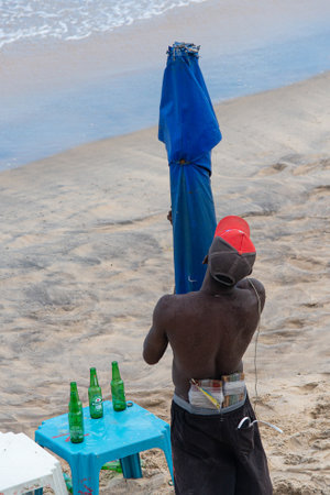 Salvador, Bahia, Brazil - June 15, 2019: A street vendor is seen on the beach placing an umbrella for tourists to protect themselves from the sun in the city of Salvador, Bahia.のeditorial素材