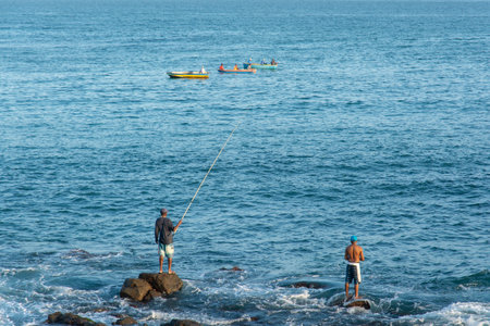 Salvador, Bahia, Brazil - July 06, 2019: Fishermen are seen on top of the rocks at Paciencia beach fishing with rods in the city of Salvador, Bahia.のeditorial素材