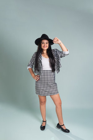 Young beautiful woman standing in studio posing for photo. Wearing and holding a black hat. Calm woman at ease wearing black and white clothing. Isolated on light green background.の写真素材