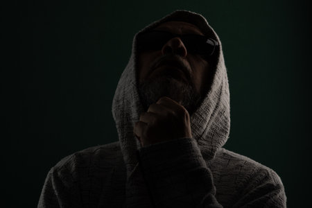 Silhouette of mysterious man wearing sunglasses and hooded sweatshirt covering his head. Isolated on darkened background.の写真素材