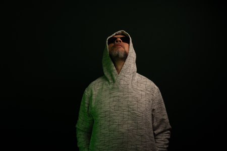 Portrait of man wearing sunglasses and hooded sweatshirt looking up. Isolated on dark background.の写真素材