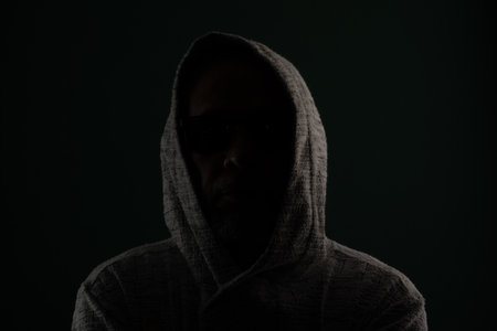 Silhouette of mysterious man wearing sunglasses and hooded sweatshirt covering his head. Isolated on darkened background.の写真素材