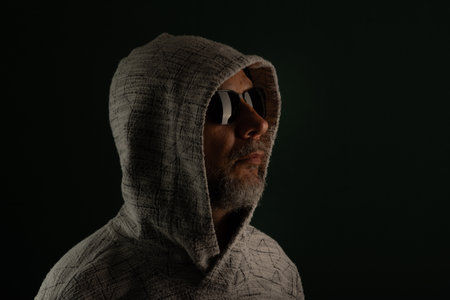 Mysterious man wearing sunglasses and hooded sweatshirt covering his head. Isolated on darkened background.の写真素材