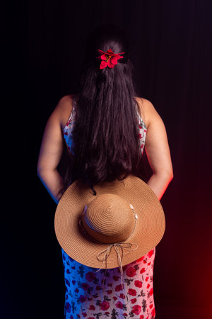 Beautiful young woman with her back to the camera wearing colorful dress holding a hat with her hand. Isolated on colorful smoky background.の写真素材