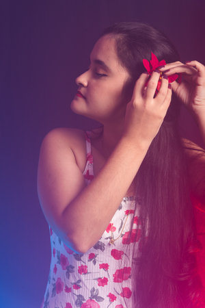 Black haired woman wearing colorful dress holding red flower on left ear. Isolated on colorful smoky background.の写真素材