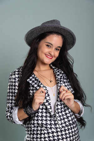 Portrait of beautiful smiling woman looking at the camera wearing a gray hat with black and white clothes. Isolated on light green background.の写真素材