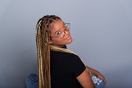 Brunette woman with braids in her hair, wearing a black blouse and wearing glasses, sitting on the...