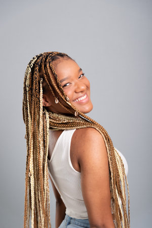 Beautiful brunette woman with braids in her hair wearing jeans and white shirt looking and smiling at the camera. Isolated on gray studio background.の写真素材