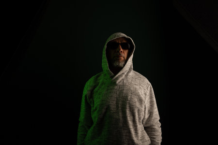 Man wearing sunglasses and hooded sweatshirt covering his head posing for the camera. Isolated on...