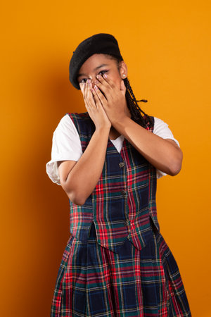 Brunette teenager wearing black beret with braids in her hair, standing with hands on her face....