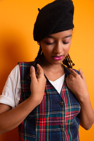 Portrait of brunette teenage girl wearing black beret with braids in her hair, smiling and happy posing for photo. Isolated on yellow background.の写真素材