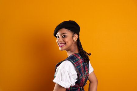 Portrait of beautiful brunette teenage girl wearing black beret with braids in her hair, smiling and happy posing for photo. Isolated on yellow background.の写真素材